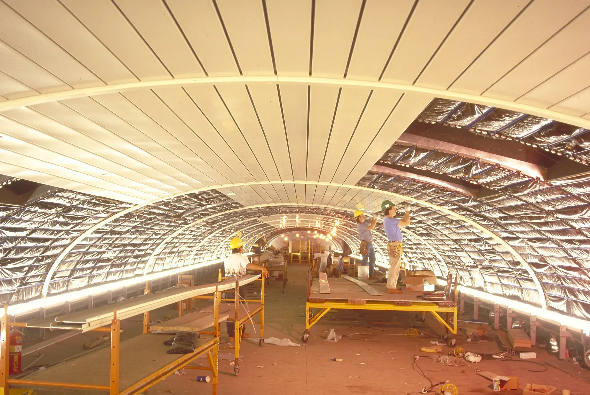 Construction workers install ceiling panels in the Penn Station. The wide-angle perspective shows the curved ceiling.