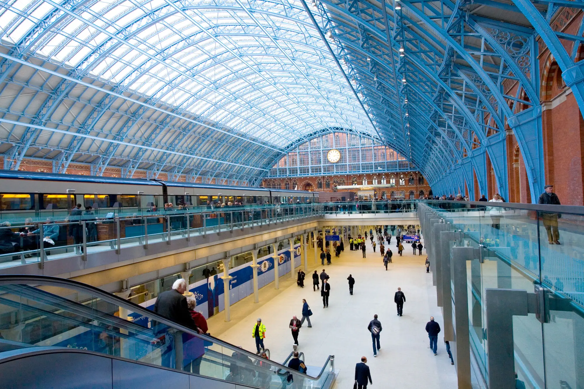 Travelers walk through the (concourse, terminal, platform, station). View down the length of the curve roof of the Barlow shed.